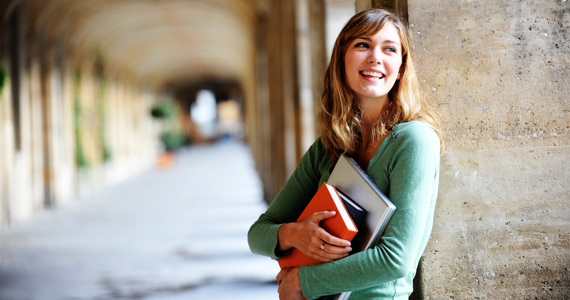 Young woman on university campus smiles while holding her books in her arms